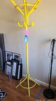 Full height view of the yellow metal coat rack showing its hook arrangement and structural design.