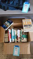 Box containing multiple computer and SQL related books with one open book Lean Analytics on top.