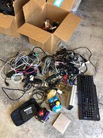Top view of open box with tangled computer cables, wired keyboards, mice and various accessory parts on floor