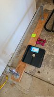 Photo showing the metal chin-up bar mounted on a wooden plank, black digital scale on floor beside pink hand weights