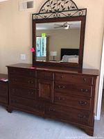 Front view of dresser with attached framed mirror and decorative metal scrollwork on top of mirror.