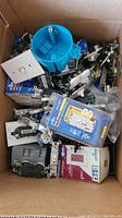 View inside box showing multiple electrical components including white switch plates, light switches, sockets, and a blue electrical box. Mixed new and used items.