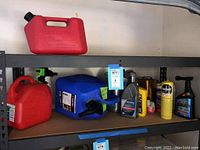 Shelf with three plastic fuel cans and various motor oils and chemicals.