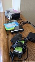 Photo showing Fujifilm camera, black portable hard drive, black device possibly battery charger, power adapters with cords.