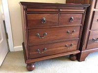Front view of the wooden nightstand showing four drawers with metal handles and bun feet.