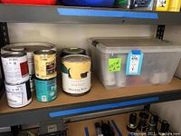 Paint cans and plastic container with spray paint cans on shelves