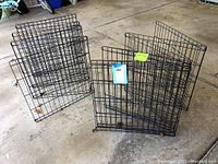 Two sets of metal wire pet enclosure panels arranged on a concrete floor, clearly showing the black wire grid construction with hooks connecting panels.