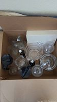 Overhead photo showing various clear glass jars, bowls, and bottles inside a cardboard box.