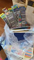 Photo showing various colorful packs of bulletin board borders, crayons, and paper materials inside a clear plastic bag within a fabric tote.