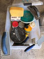 View of lot showing assorted tile tools including grout float, sponges, spatulas, trowels, and multiple containers of grout or adhesive.