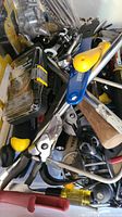 Photo showing mixed tools including pliers with yellow handles, metal wrenches, screwdriver tips, and other small hand tools in a pile.
