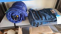 Photo showing rolled blue sleeping bag and dark blue GoRuck backpack on a table.