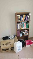 Full view of oak bookshelf on neutral wall with items on floor including Dual HiFi box, white plastic container, and pink box