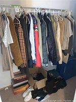 Hanging men's shirts, jackets, and coats in various colors and patterns on a rack along with some items on the floor below including a pair of white sneakers.