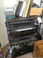 Full view of black metal shelf loaded with four AV components and cables on floor