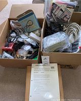 Two medium boxes filled with assorted electronic items including cables, adapters, Heathkit manual and dust cover packaging.