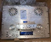 Top-down view of unit inside box showing dual reel spindles, front panel controls and blue display