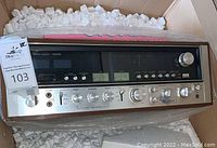 Front view of Sansui 9090DB in cardboard box with packing peanuts showing speaker selector, headphone jack and tone controls.