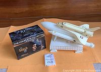 White NASA space shuttle model with external fuel tank and boosters on white stand, alongside boxed DVD set 'In Search Of' hosted by Leonard Nimoy.