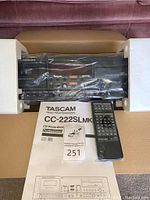 Front view of TASCAM CC-222SLMkII unit in foam inserts, sealed in plastic, remote and manual visible