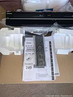 Front view of Toshiba DVR670KU combo unit with styrofoam inserts, remote in plastic and owner’s manual laid out