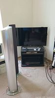 Wide shot of TV stand with TV, one tower speaker partially visible left