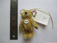 Mini Steiff mohair bear with tags and button, held with ruler showing about 4 inch height.