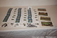 Photo showing rows of multiple First Day Covers displayed alongside packs of postcards and additional envelopes on a table.