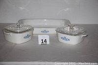 Three CorningWare Blue Cornflower pattern ceramic cookware pieces including two casseroles with lids and one roaster without lid all displayed from the front on plain background.