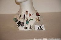 Photo showing a display bust with the 15 assorted handmade pendants hung on a sterling silver chain around the neck. Various shapes and colors are visible including animals, stones, and symbolic pendants.