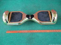 Full view of the Powerboard hoverboard showing gold finish, black footpads, and length measurement with ruler.