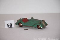 Side angle showing the green steel toy car with red interior and wind-up key laying in front.