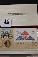 Photo showing the official presentation slipcase with gold embossed title and the coin and stamp collector's set displayed inside a windowed mount card.