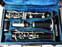 Open clarinet case showing dark wood clarinet in 4 pieces with silver keys, set in blue velvet lined custom compartments.