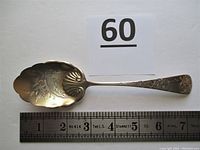 Side view of the spoon showing engraved fancy cut flower design, bowl with scalloped edges and slight gold wash.