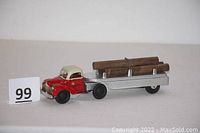 View of the entire toy logging truck showing red and cream truck cab with silver trailer carrying three wooden logs chained in place.