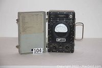 Closed metal carrying case with ME-9B/U multimeter inside showing analog needle gauge and control knobs.