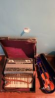 Vintage accordion in maroon velvet-lined case, showing wear on case edges and accordion keyboard