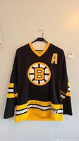 Front view of black Bobby Orr Boston Bruins hockey jersey with yellow and white trim, showing Bruins logo and alternate captain 'A' patch.