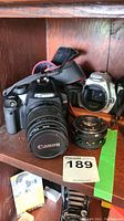 Photo showing Canon EOS Rebel XSi with lens and Rebel 2000 camera body on wooden shelf with lot tag