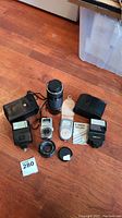 Full lot view showing all items: two Canon lenses, two Canon flashes, two handheld light meters on wooden floor.