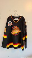 Full front view of black Canucks jersey on hanger