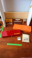 Four cleaning kits for hunting tools on wood table including two metal/plastic cases and two cardboard boxes