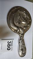 Full view of silver-tone dragon hand mirror showing back and handle with dragon design.