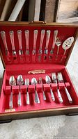 Full view of the Community flatware set with 37 pieces and 2 other pieces in a red fabric lined wooden box.