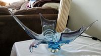 Blue and purple abstract glass art sculpture on a white cloth with a living room background.