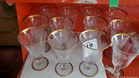 View of 12 etched glasses with gold rim sitting on a red shelf, showing their shape and arrangement.