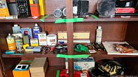 Shelf display with assorted items including cans of Brasso and other liquids, small tools, boxes, and books.