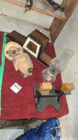 Multiple items on a red carpet including a coconut figurine, wooden mantle clock, oil lamp, and pair of magazine holders.