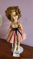 Full view of Shirley Temple doll standing with pink dress and curly hair.
